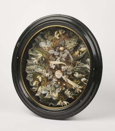 Totengedächtnis: Verglaster Holzkasten mit künstlichen weissen Blumen und Gräsern zum Andenken an den verstorbenen Johann Baumgartner (1848–1886)